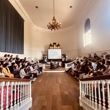 two speakers sat in front of a audience giving a talk
