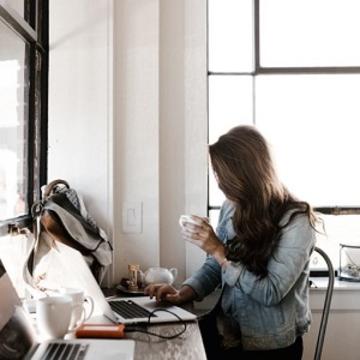 Woman holding a coffee cup working at a laptop at a desk
